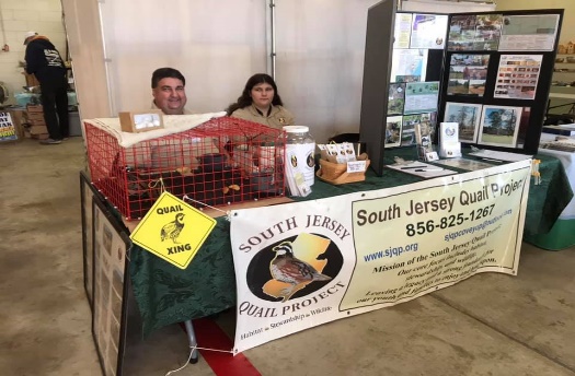 Two people sit behind a table that has a SJQP banner on the front 
